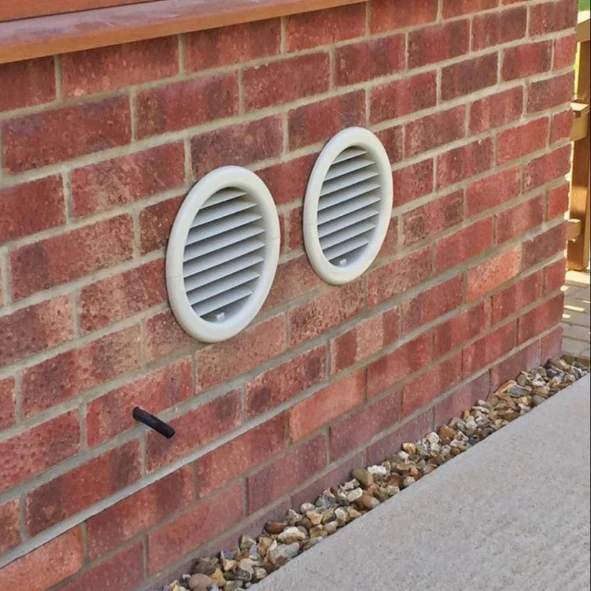 Twee ronde monoblock-aircoroosters en een kleine doorvoer in een bakstenen gevel